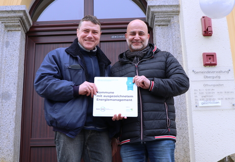 Bürgermeister und Energiemanager aus Obergurig halten Kom.EMS Schild